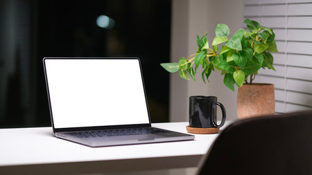 Laptop, coffee cup and potted plant on white table at night. Empty screen for your advertise design.の写真素材