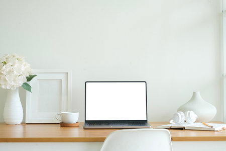 Front view laptop with blank white screen, books, coffee cup and picture frame on wooden table.の写真素材