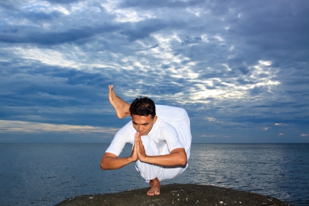 Portrait of Asian young man doing yoga exercise on stone with cloudy sky and ocean, Thailandの写真素材