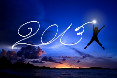 Young man jumping and drawing 2013 on the beach before sunrise skyの写真素材