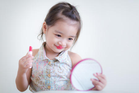 Little girl with mirror doing makeup at her houseの写真素材