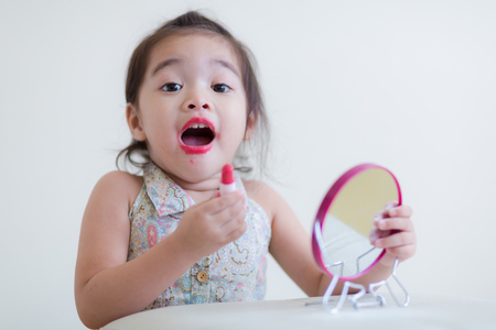 Little girl with mirror doing makeup at her houseの写真素材