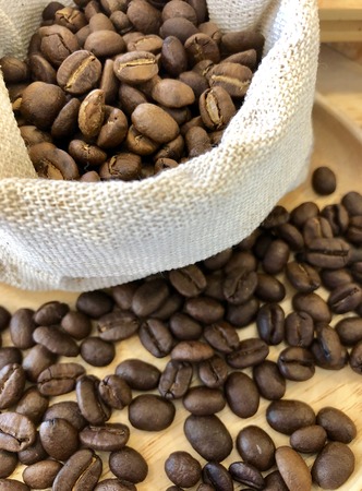 Freshly roasted coffee beans In a cloth bag on a wooden floor.の写真素材