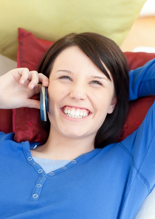 Laughing young woman talking on phone lying on a sofaの写真素材