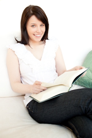 Cheerful woman reading a book sitting on a sofaの写真素材