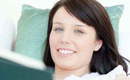 Cheerful woman reading a book lying on a sofa の写真素材