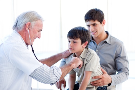 Senior doctor examining a little boy with his fatherの写真素材