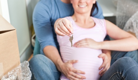 Close-up of a lovely couple expecting a baby sitting on the floor and holding the key of their new hの写真素材