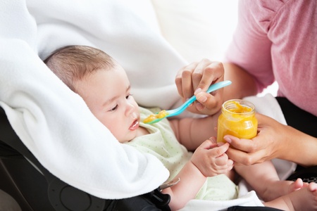 Close-up of a young mother giving carrot puree to her baby for lunch in the living-roomの写真素材