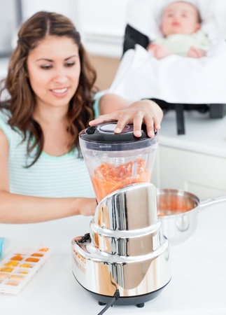 Beautiful mother mixing carrot with a blender for her baby lunchの写真素材
