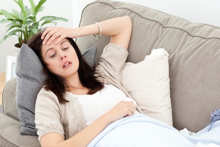 Indisposed woman feeling her temperature while resting on the sofa Indisposed woman feeling her temperature while resting on the sofa
