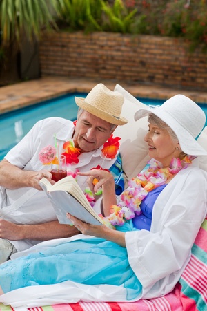 Mature woman reading a book while her husband is drinking a cocktailの写真素材
