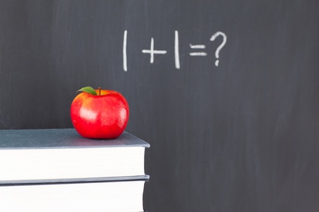 Stack of books with a red apple and a  blackboard with 1+1=? written on it