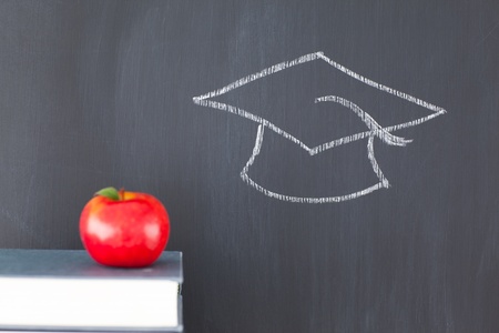 Stack of books with a red apple and a blackboard with a graduation cap drawn on itの写真素材