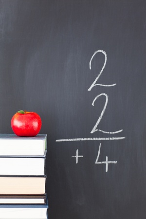Stack of books with a red apple and a blackboard with a simple fraction written on itの写真素材