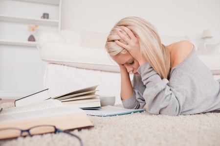 Attractive blond woman frustrated with her books lying on a carpet in the living room