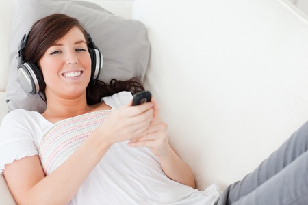 Attractive brunette woman writing a text on her mobile while lying on a sofa in the living roomの写真素材