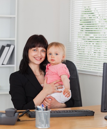 Attractive brunette woman posing while holding her baby on her knees in the officeの写真素材
