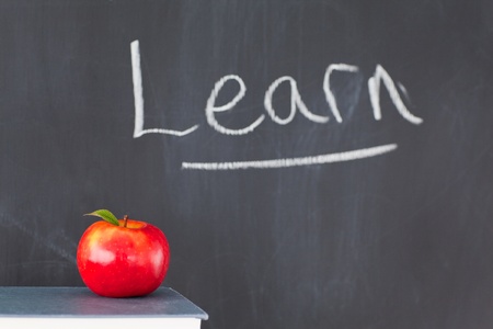 Stack of books with a red apple and a blackboard with "learn" written on itの写真素材