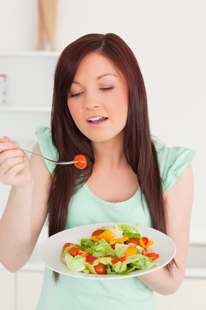 Pretty red-haired woman enjoying a mixed salad in the kitchen in her apartmentの写真素材
