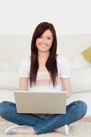 Attractive woman relaxing with her laptop while siting on a carpet in the living roomの写真素材