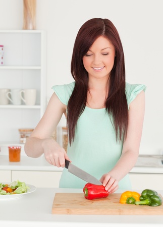 Gorgeous red-haired woman cutting some vegetables in the kitchen in her appartmentの写真素材