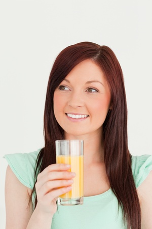Glad red-haired woman enjoying a glass of orange juice in the kitchen in her apartmentの写真素材