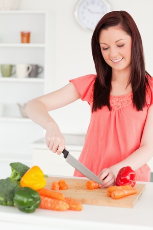 Attractive red-haired woman cutting some carrots in the kitchen in her appartmentの写真素材