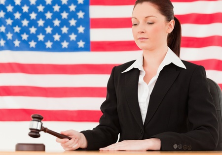 Serious young judge knocking a gavel with an American flag in the backgroundの写真素材