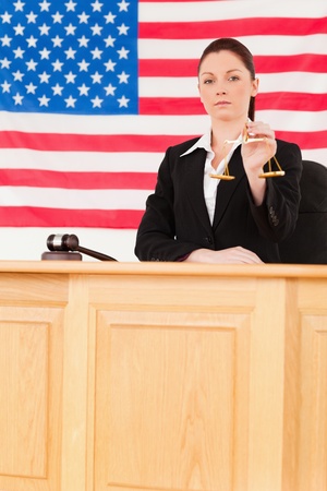 Cute judge holding scales of justice with an American flag in the backgroundの写真素材