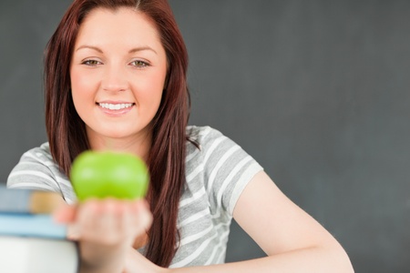 Cute young student showing an apple in a classroomの写真素材