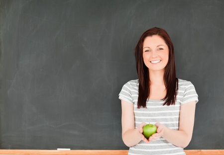 Beautiful young woman holding an apple against a blackboard in a classroomの写真素材