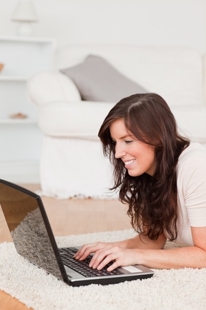 Good looking brunette woman relaxing with her laptop while lying on a carpet in the living roomの写真素材