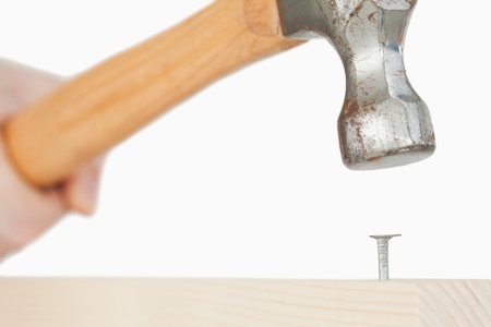 Hand holding a hammer to drive a nail into a wooden board with the camera focus on the nailの写真素材