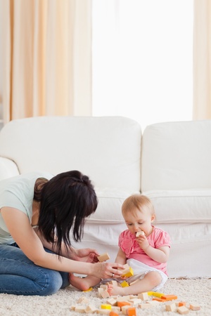 Beautiful woman playing with her baby in while sitting on a carpet in the living roomの写真素材