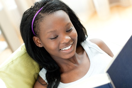 Smiling woman reading a book lying on a sofaの写真素材