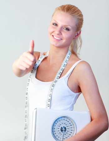 Attractive woman with thumb up holding a scales focus on womanの写真素材