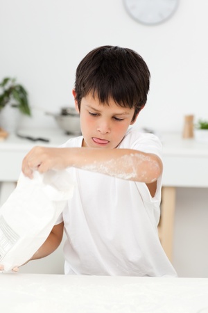 Cute boy pouring flour on a table in his kitchenの写真素材