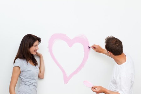 Cute woman looking at her boyfriend painting a heartの写真素材