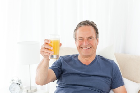 Retired man looking at the camera while he is drinking oranje juice at homeの写真素材