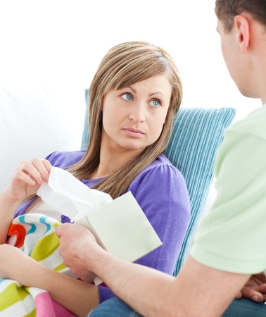 Assertive man giving his ill girlfriend tissue lying on a sofa Assertive man giving his ill girlfriend tissue lying on a sofa