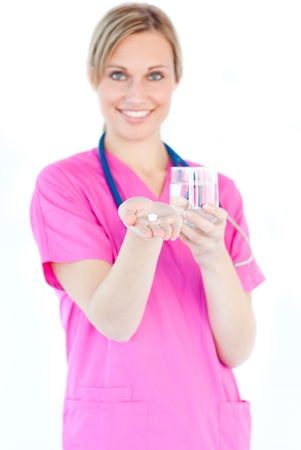 Bright female nurse holding pills and a glass water smiling at the camera の写真素材