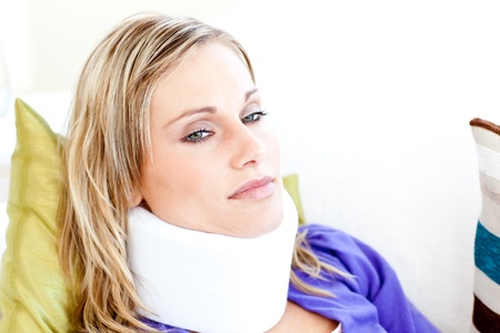 Beautiful woman wearing neckbrace lying on a sofaの写真素材