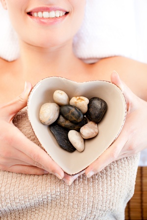 Close-up of a smiling woman holding a bowl in the shape of a heart with pebblesの写真素材