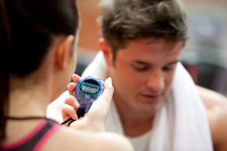 Female trainer holding a chronometer while man doing physical exerciseの写真素材