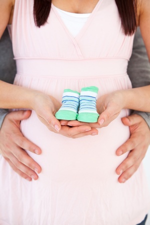 Close-up of the belly of a pregnant woman holding baby shoes and of her husbandの写真素材