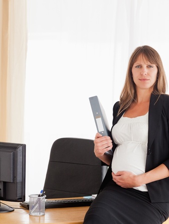 Lovely pregnant female holding a file while standing in the officeの写真素材