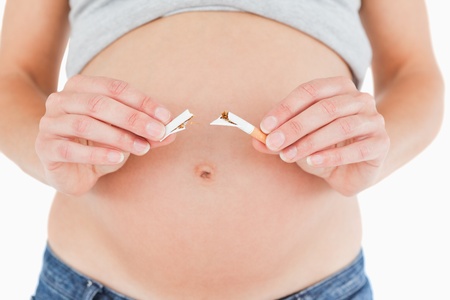 Young pregnant woman holding a broken cigarette while standing against a white backgroundの写真素材