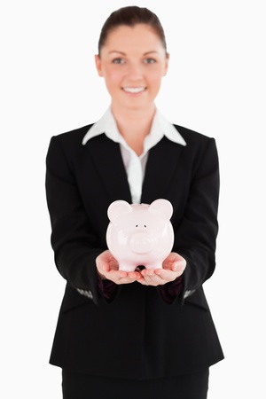 Beautiful woman in suit holding a pink piggy bank while standing against a white backgroundの写真素材