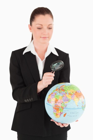 Good looking female in suit holding a globe and using a magnifying glass while standing against a white backgroundの写真素材